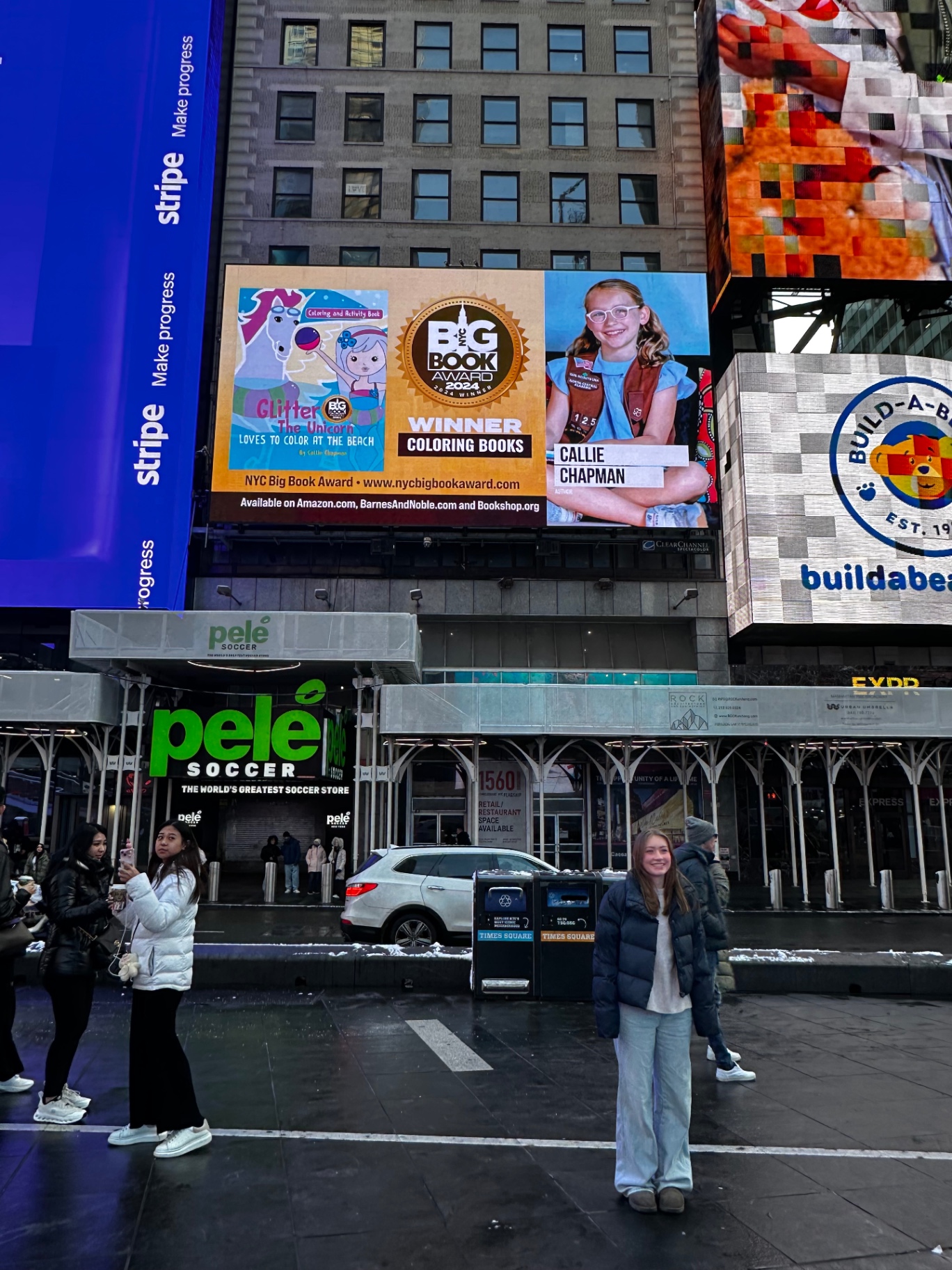 Callie standing under her Glitter the Unicorn billboard in Times Square
